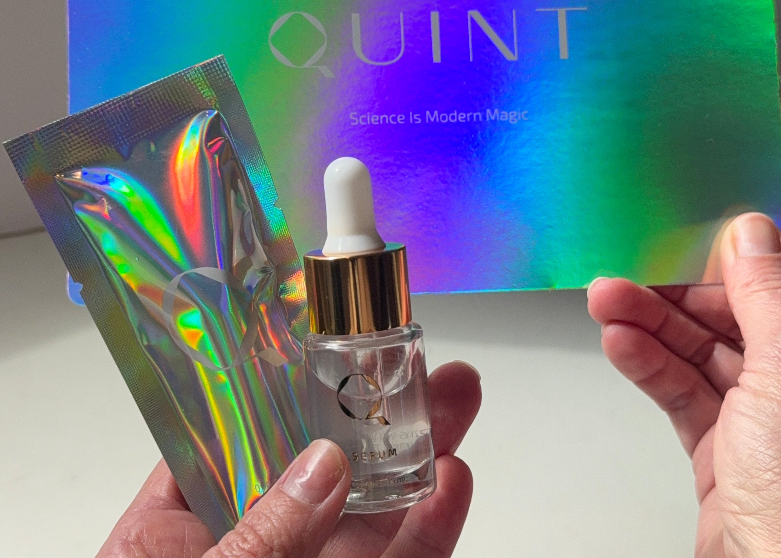 Hand holding a small dropper bottle over a colorful 'QUINT' package.